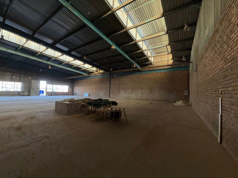 Spacious industrial warehouse featuring exposed brick walls, high steel truss ceilings with integrated skylights, and durable concrete flooring, suitable for various commercial or storage uses.