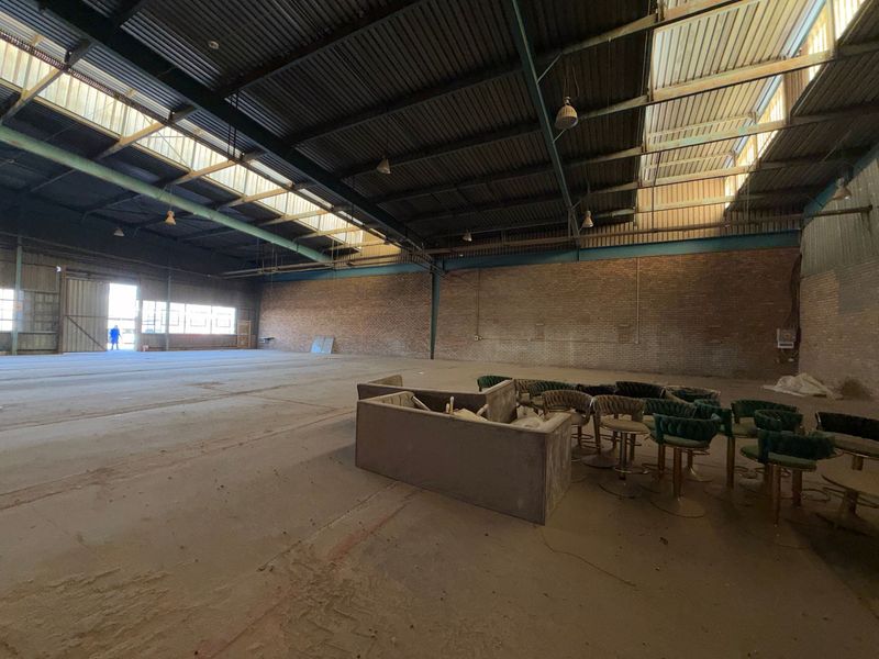 Spacious industrial warehouse featuring exposed brick walls, high steel truss ceilings with skylights, and durable concrete flooring, suitable for various commercial or storage uses.