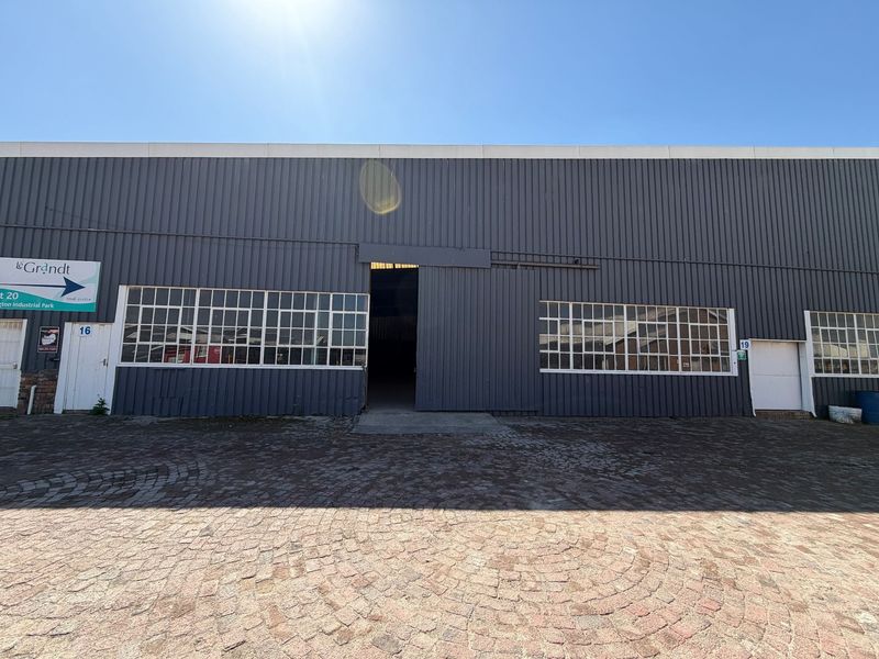 Front elevation of an industrial warehouse unit featuring dark corrugated metal cladding, large multi-pane windows, and a central sliding access door.