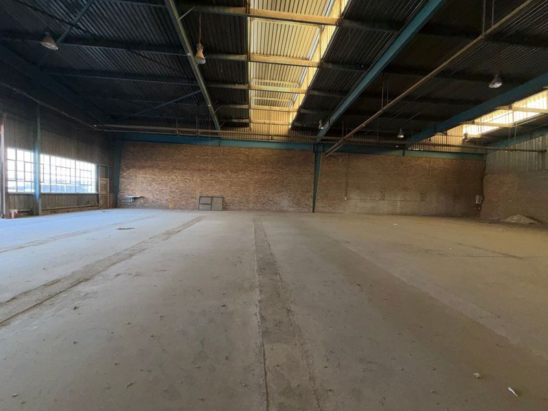 Spacious industrial warehouse featuring exposed brick walls, high steel truss ceilings with integrated skylights, and durable concrete flooring, suitable for various commercial or storage uses.