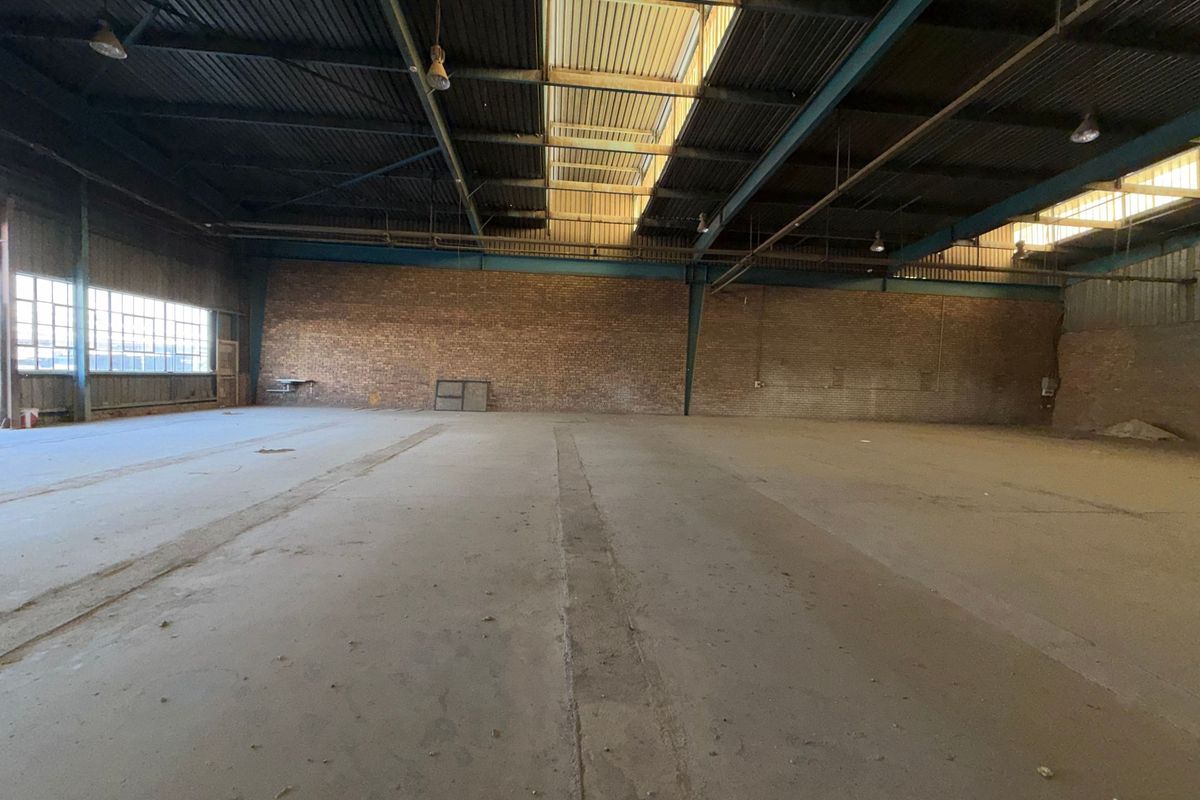 Spacious industrial warehouse featuring exposed brick walls, high steel truss ceilings with integrated skylights, and durable concrete flooring, suitable for various commercial or storage uses.