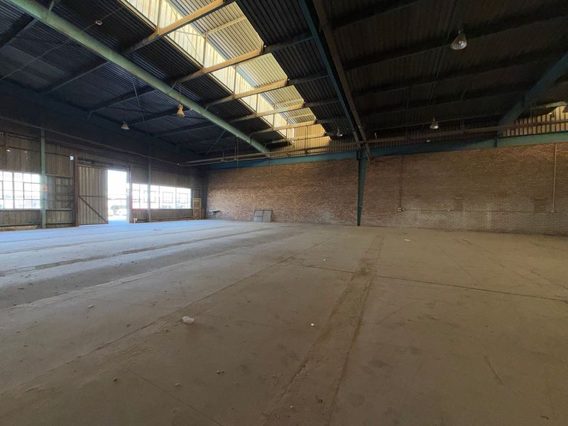 Spacious industrial warehouse featuring high ceilings with skylights, exposed steel trusses, durable brick walls, and expansive concrete flooring.