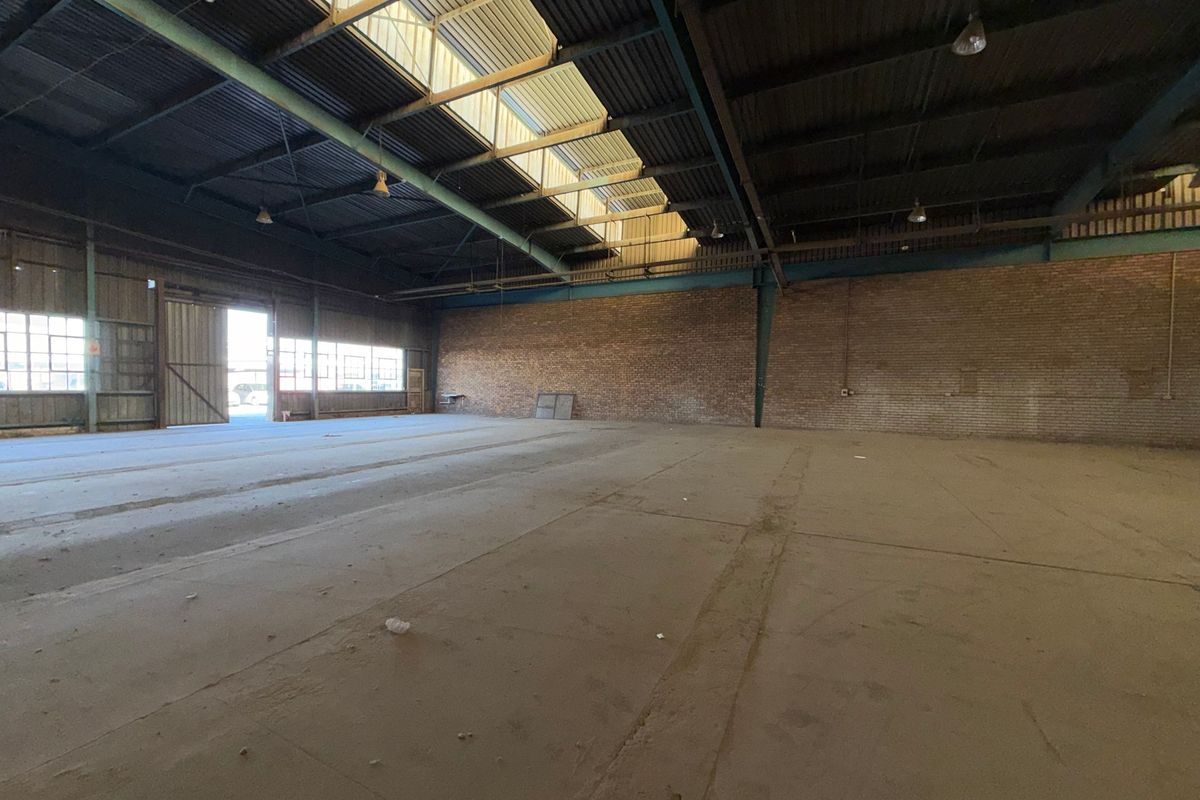 Spacious industrial warehouse featuring high ceilings with skylights, exposed steel trusses, durable brick walls, and expansive concrete flooring.
