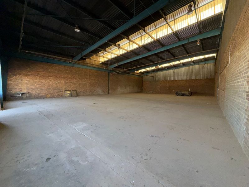 Spacious industrial warehouse unit featuring exposed brick walls, high steel truss ceilings with skylights, and durable concrete flooring, suitable for various commercial or storage uses.