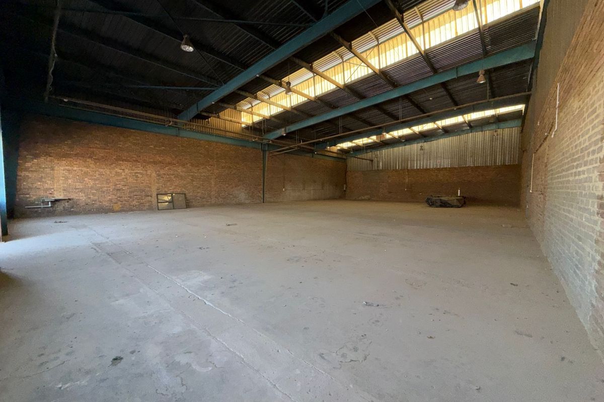 Spacious industrial warehouse unit featuring exposed brick walls, high steel truss ceilings with skylights, and durable concrete flooring, suitable for various commercial or storage uses.
