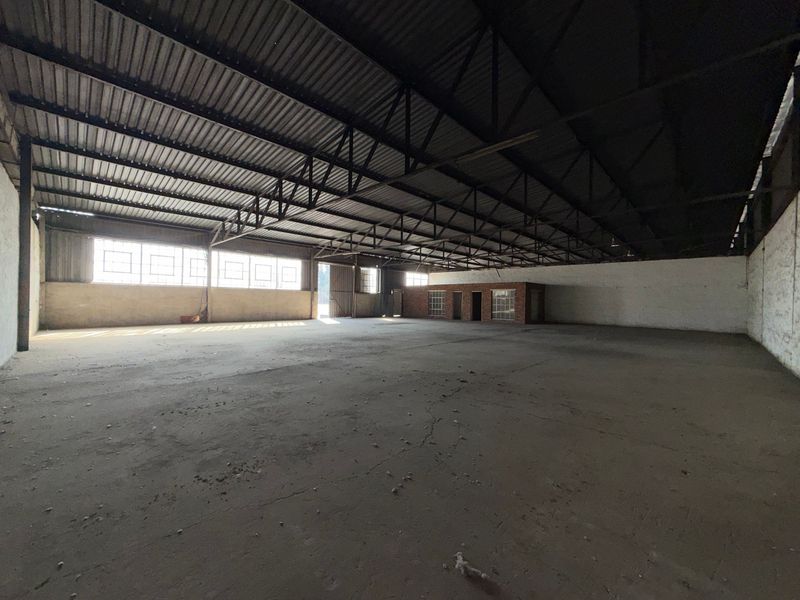 Spacious industrial warehouse featuring high exposed steel roof trusses, concrete flooring, and an integrated brick office structure, offering versatile open-plan utility space.