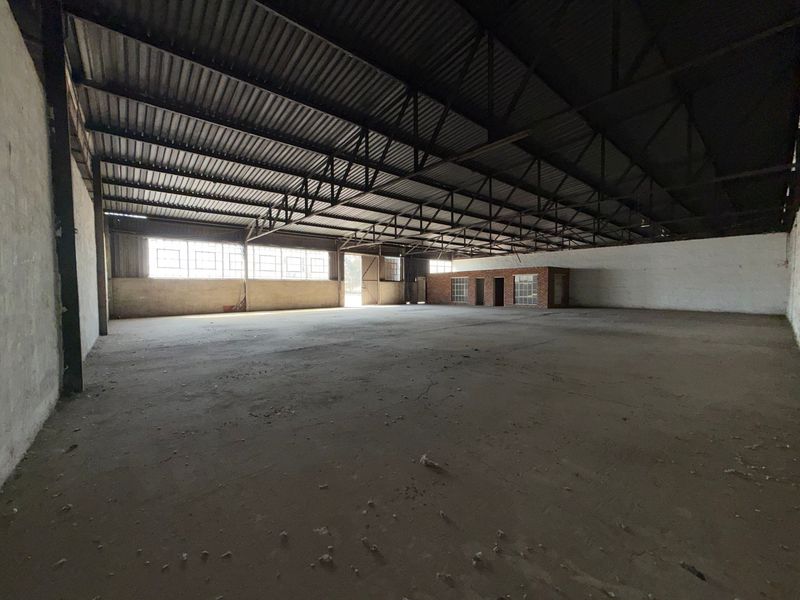 Large, open-plan industrial warehouse space featuring exposed steel roof trusses, concrete flooring, and natural light through industrial-style windows.