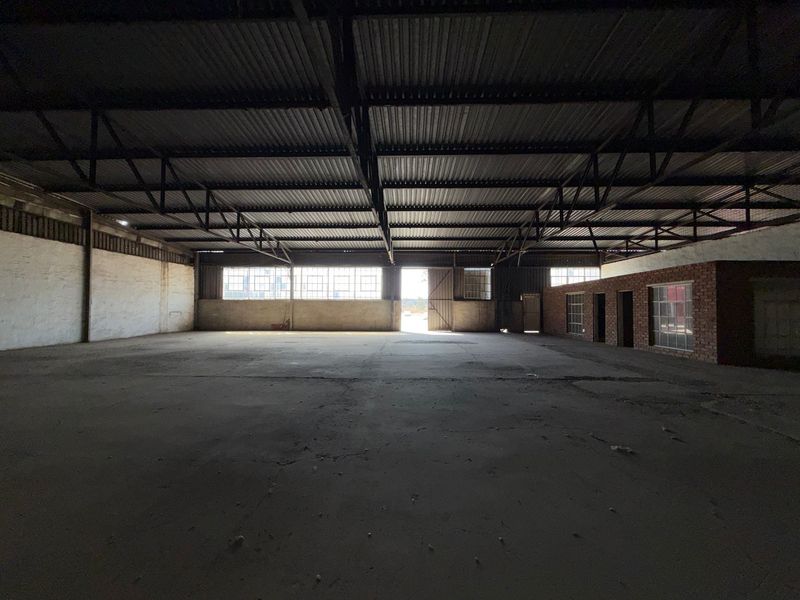 Spacious industrial warehouse featuring exposed steel roof trusses, concrete flooring, and large steel-framed windows, offering a versatile open-plan layout for various commercial uses.