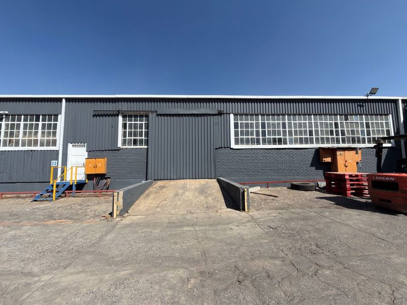 Industrial warehouse exterior featuring a large sliding door, dedicated loading ramp, steel-framed windows, and durable corrugated metal and brick facade construction.