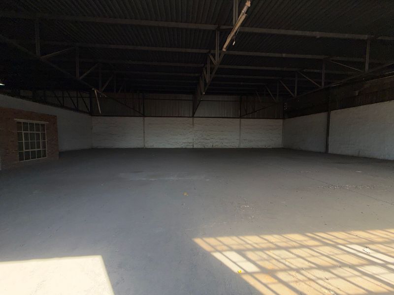 Spacious industrial warehouse unit featuring high ceilings with exposed steel trusses, concrete flooring, and masonry walls, suitable for various commercial or storage applications.