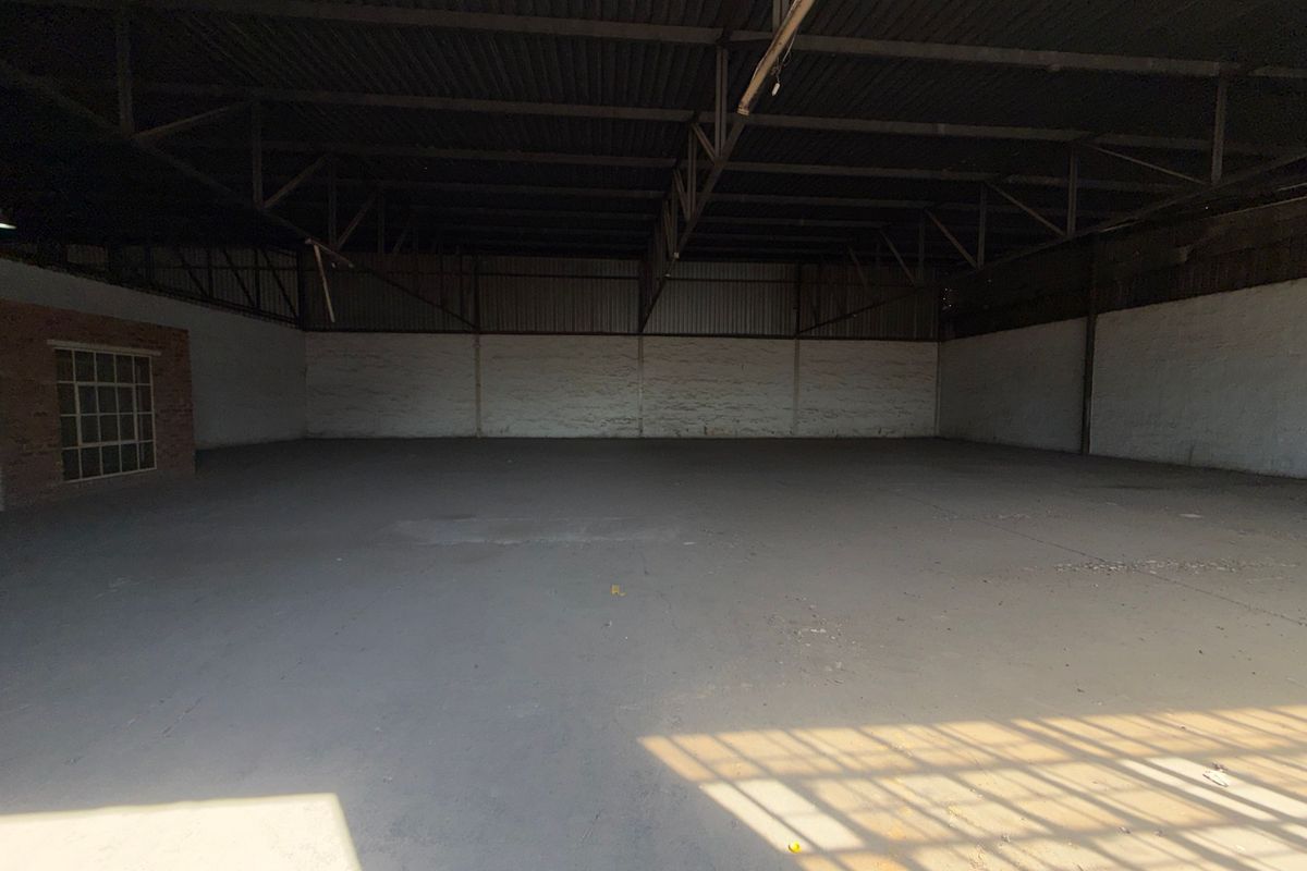 Spacious industrial warehouse unit featuring high ceilings with exposed steel trusses, concrete flooring, and masonry walls, suitable for various commercial or storage applications.
