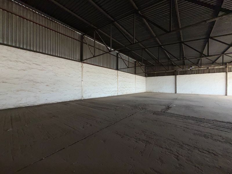 Spacious industrial warehouse unit featuring high ceilings with exposed steel trusses, durable concrete flooring, and solid masonry wall construction.