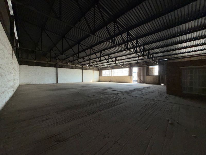 Spacious industrial warehouse unit featuring high ceilings with exposed steel trusses, concrete flooring, and natural light through industrial-style windows.