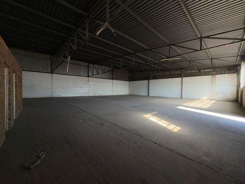 Spacious industrial utility area featuring exposed steel roof trusses, corrugated metal roofing, and durable concrete flooring, suitable for storage or workshop use.