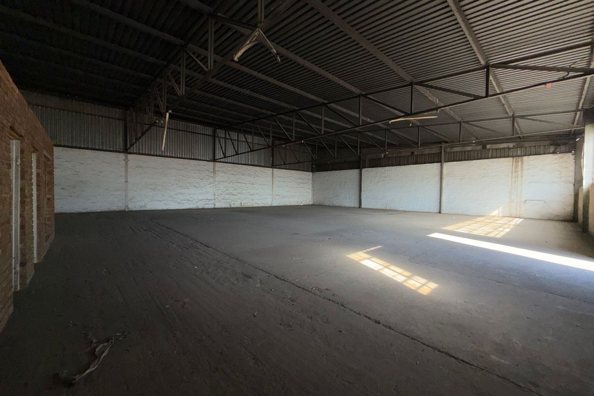 Spacious industrial utility area featuring exposed steel roof trusses, corrugated metal roofing, and durable concrete flooring, suitable for storage or workshop use.