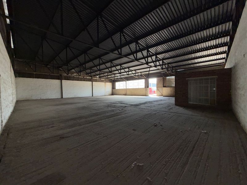 Spacious industrial warehouse featuring exposed steel roof trusses, concrete flooring, and masonry walls, offering a versatile open-plan layout for various commercial or storage uses.