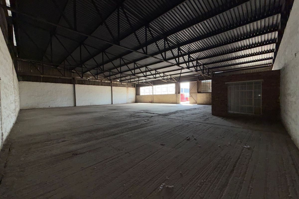 Spacious industrial warehouse featuring exposed steel roof trusses, concrete flooring, and masonry walls, offering a versatile open-plan layout for various commercial or storage uses.