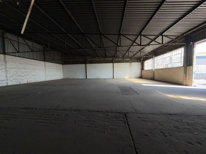 Spacious industrial warehouse unit featuring exposed steel roof trusses, concrete flooring, and large steel-framed windows providing natural light.