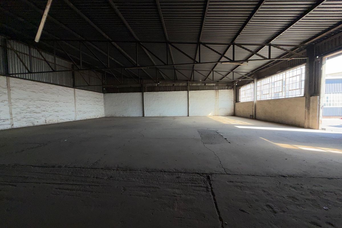 Spacious industrial warehouse unit featuring exposed steel roof trusses, concrete flooring, and large steel-framed windows providing natural light.