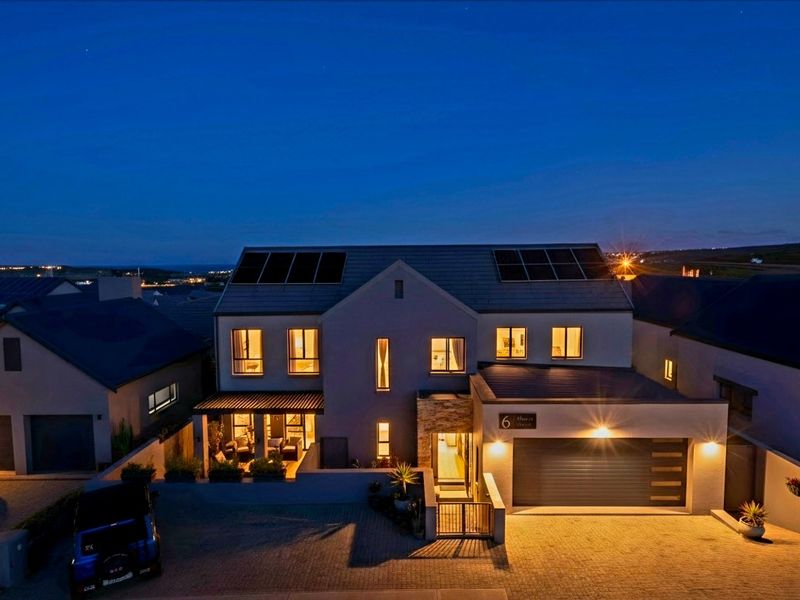 A modern double-story residential property at dusk, featuring a paved driveway, double garage, stone-clad accents, and roof-mounted solar panels.