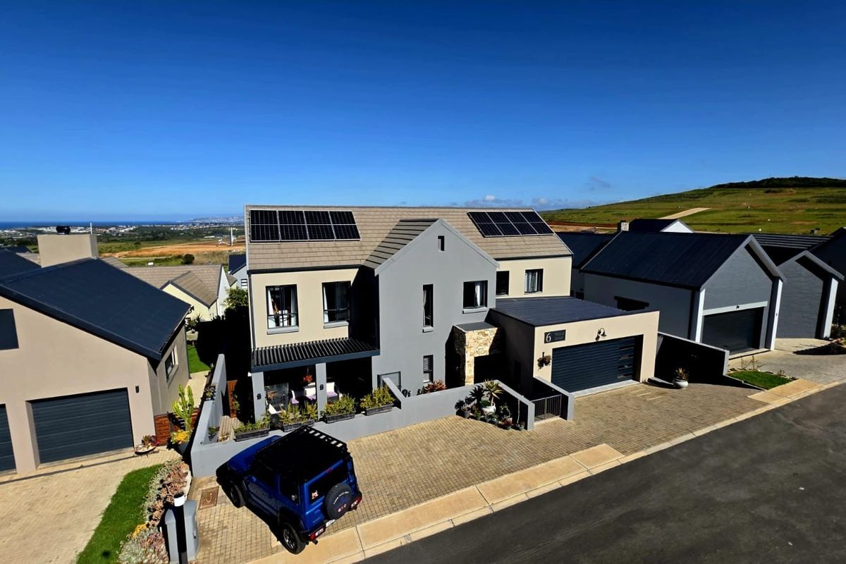 Aerial view of a modern double-story residential property featuring solar panels, a paved driveway, and a double garage in a coastal estate setting.