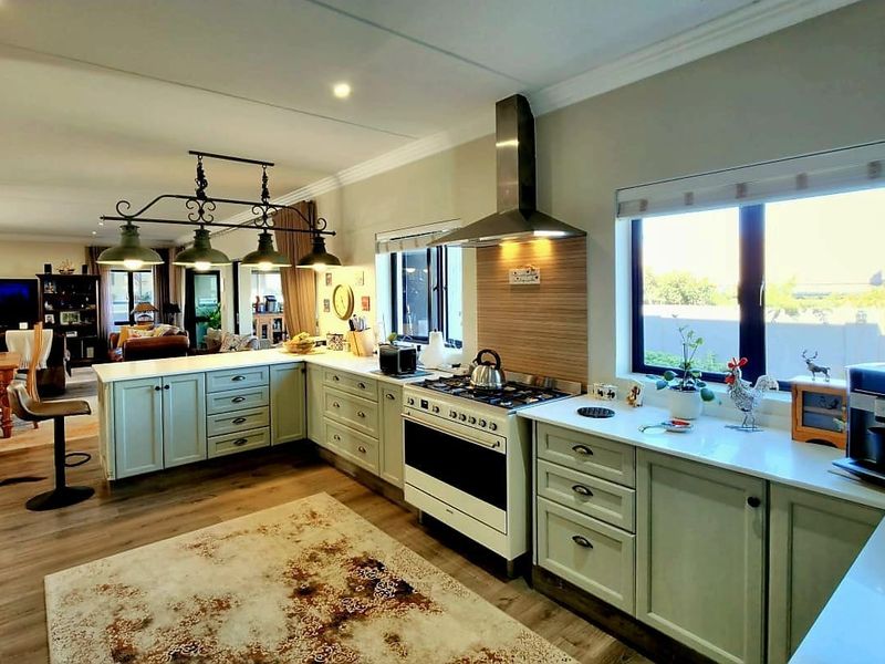 Spacious open-plan kitchen featuring light-toned cabinetry, stone countertops, a gas stove with extractor fan, and seamless flow into the adjacent living and dining area.