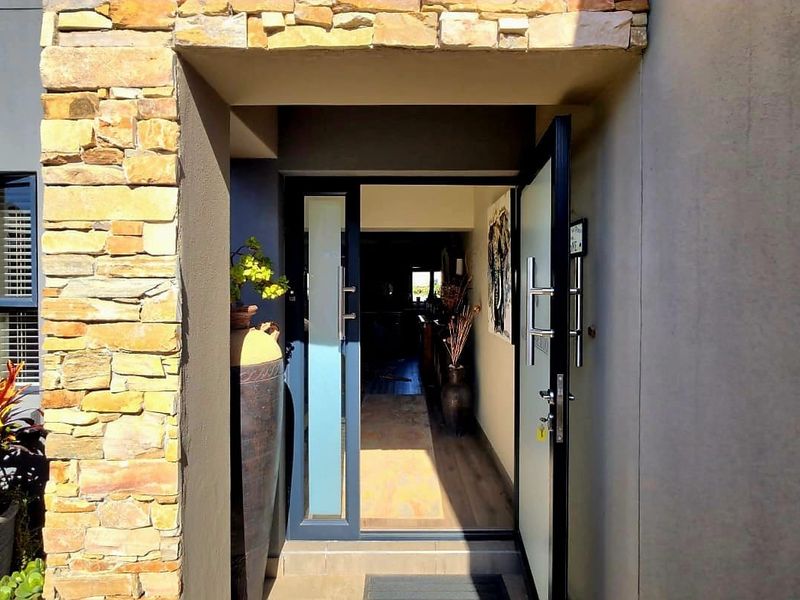 A modern entrance featuring a stylish pivot door with a glass sidelight, accented by natural stone cladding on the exterior facade.