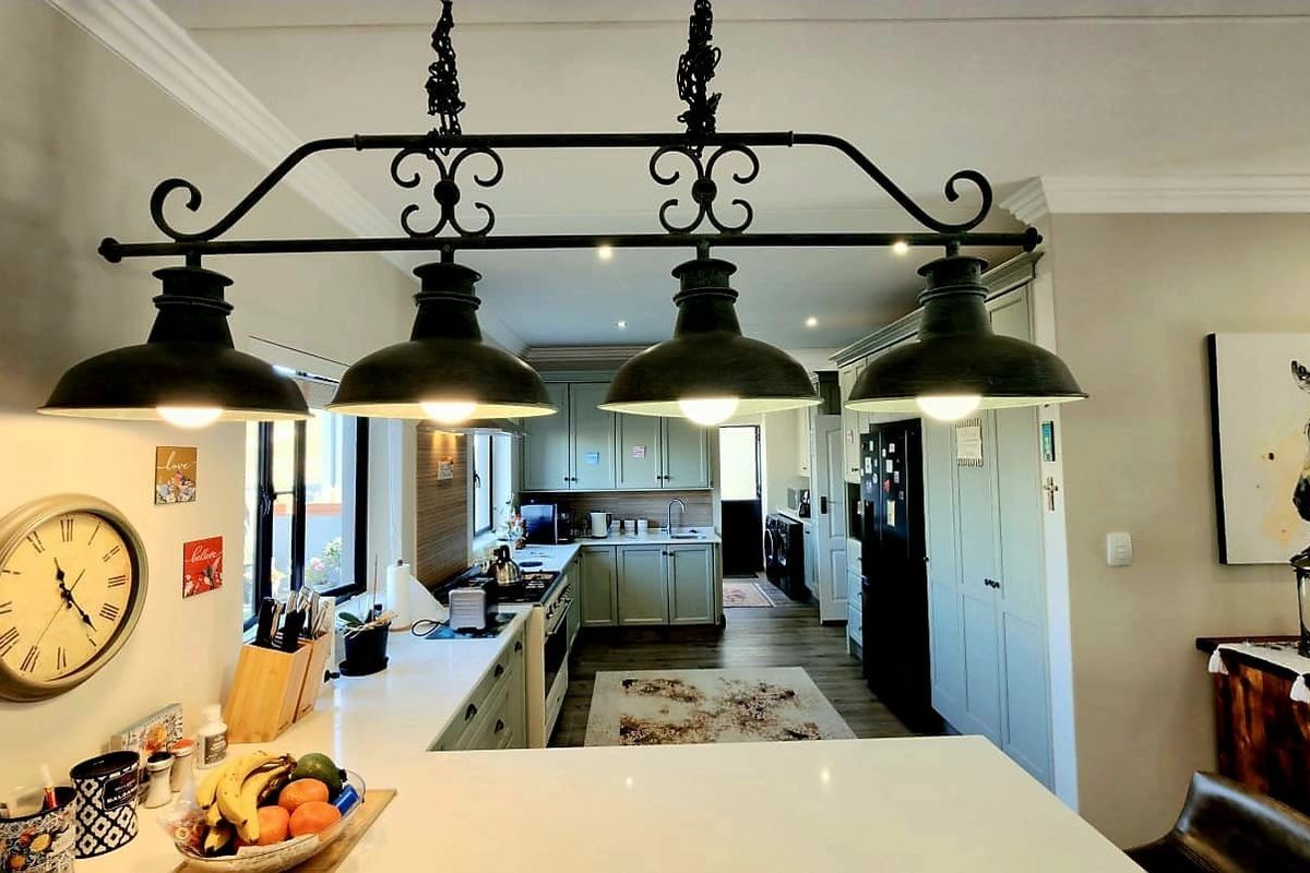 A well-appointed kitchen featuring shaker-style cabinetry, quartz countertops, and a prominent industrial-style pendant light fixture over the breakfast bar area.