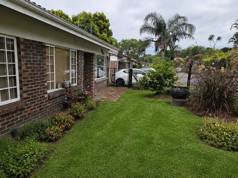 Front exterior view of a townhouse featuring a face brick facade, a well-maintained lawn, and a stone paved walkway leading to the entrance.