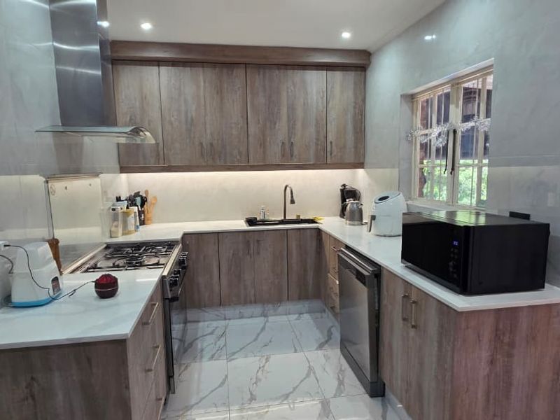 Modern kitchen featuring wood-finish cabinetry, stone countertops, gas hob with extractor, and marble-look tiled flooring, offering a clean and functional workspace.