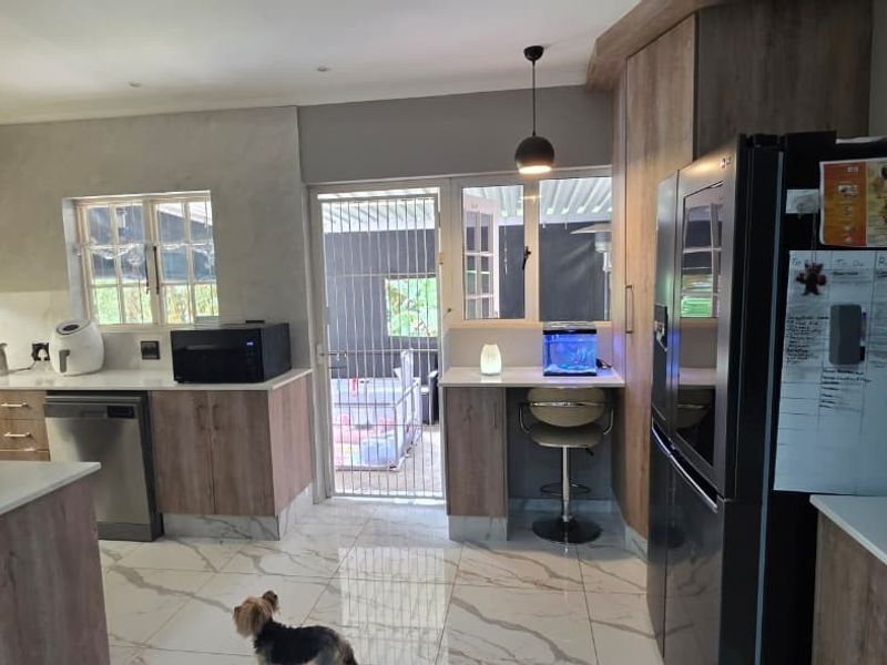 Modern kitchen featuring wood-finish cabinetry, stone countertops, tiled flooring, and direct access to an outdoor area through a secure gate.