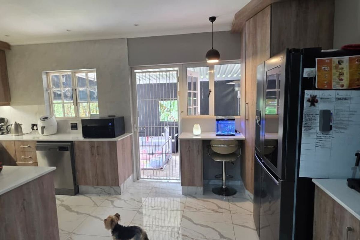 Modern kitchen featuring wood-finish cabinetry, stone countertops, tiled flooring, and direct access to an outdoor area through a secure gate.