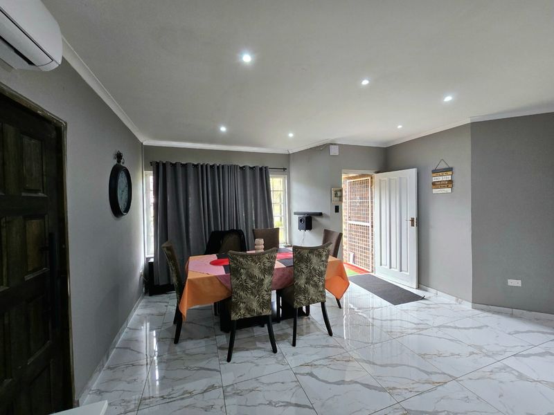 Open-plan living and dining area featuring polished marble-look floor tiles, recessed downlighting, and a wall-mounted air conditioning unit.