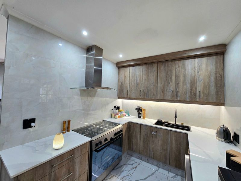 Modern kitchen featuring wood-grain cabinetry, stone countertops, gas stove with extractor fan, and high-quality tiled finishes with integrated lighting.