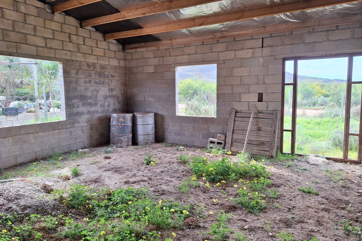 An unfinished interior space featuring exposed concrete block walls, timber rafters, and a dirt floor, offering a blank canvas for complete renovation.