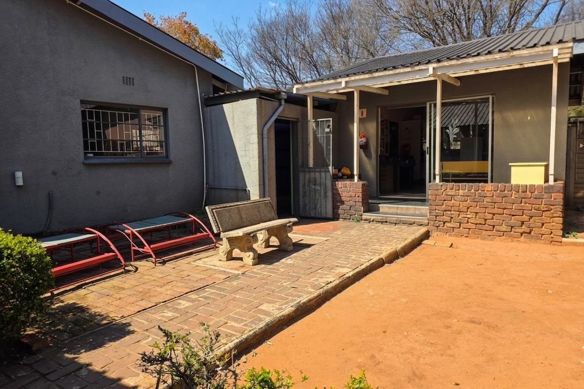Rear exterior view of the property featuring a paved patio area, covered entrance, and brick retaining wall structure.