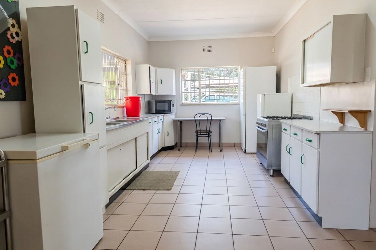 A functional kitchen featuring tiled flooring, ample built-in cabinetry, a stainless steel sink, and a freestanding stove with a tiled backsplash.