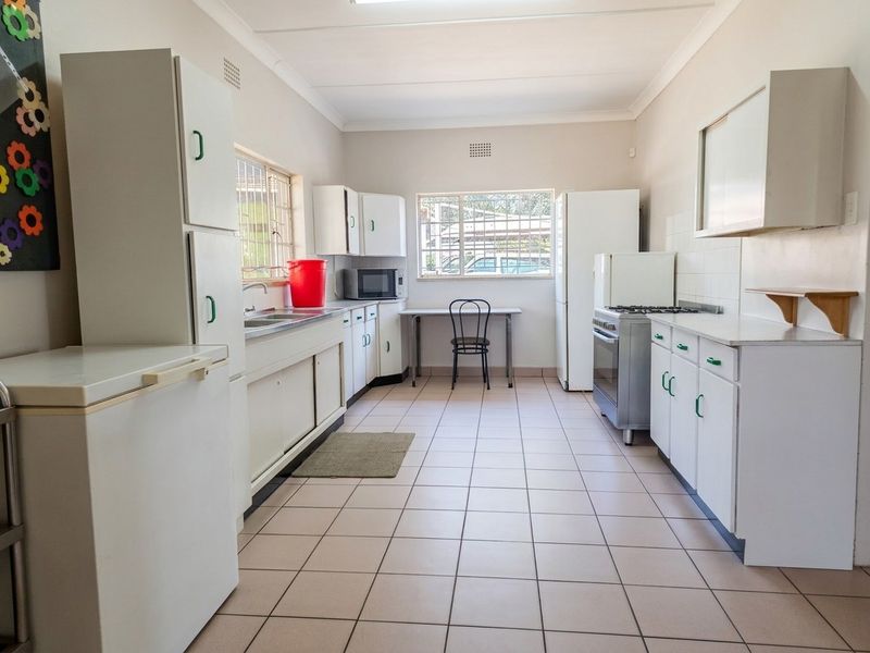 A functional kitchen featuring tiled flooring, ample built-in cabinetry, a stainless steel sink, and a freestanding stove with a tiled backsplash.