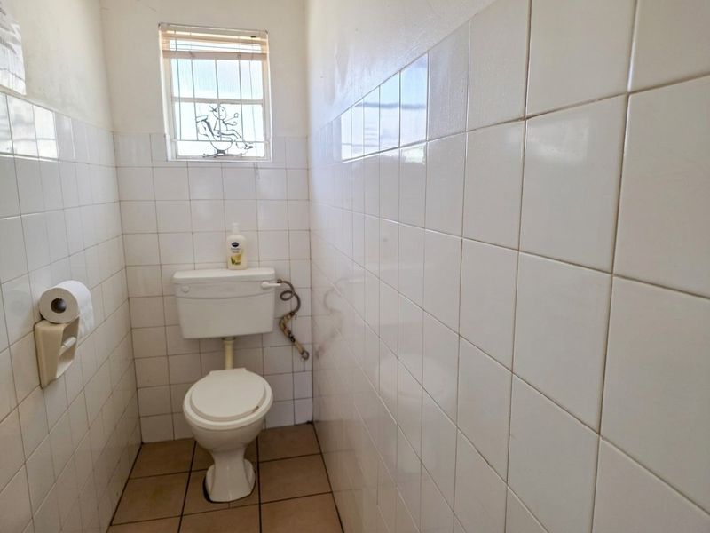 A compact, tiled bathroom featuring a standard toilet and a small window with security bars, requiring cosmetic updates to improve its overall condition.