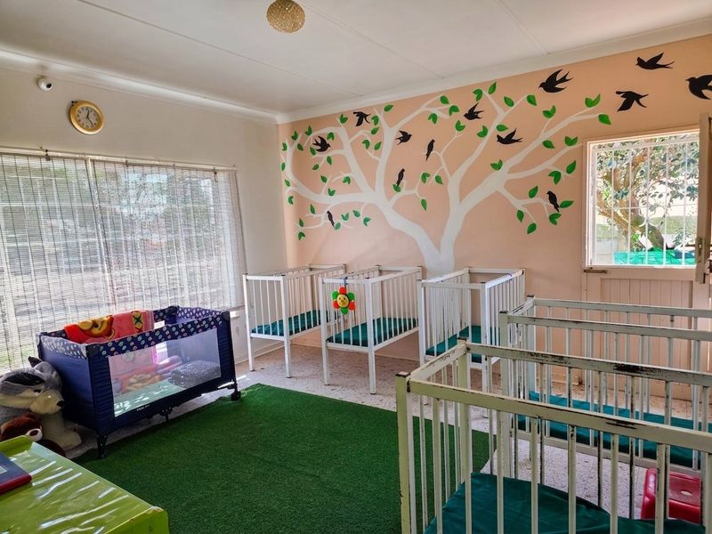 A bedroom currently utilized as a nursery, featuring painted wall murals, security gate access, and venetian blinds.
