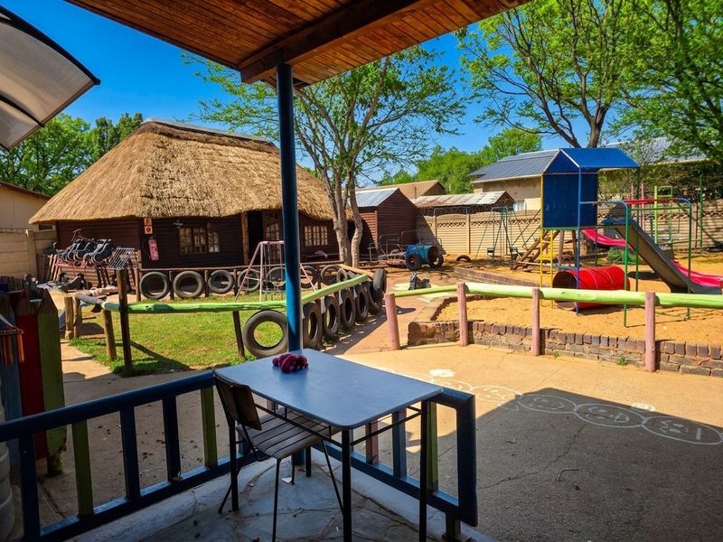 A covered patio area overlooking a large outdoor space featuring a thatched roof building and a play area.