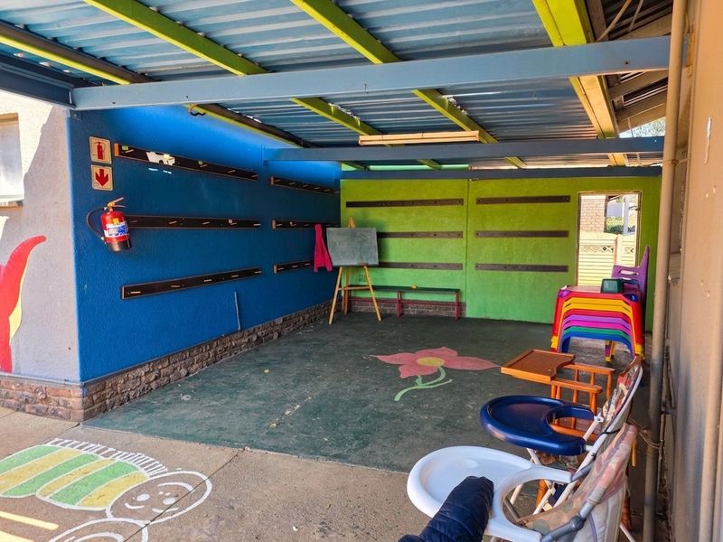 A covered outdoor patio area featuring a corrugated metal roof, concrete flooring, and brightly painted walls, suitable for a play or utility space.