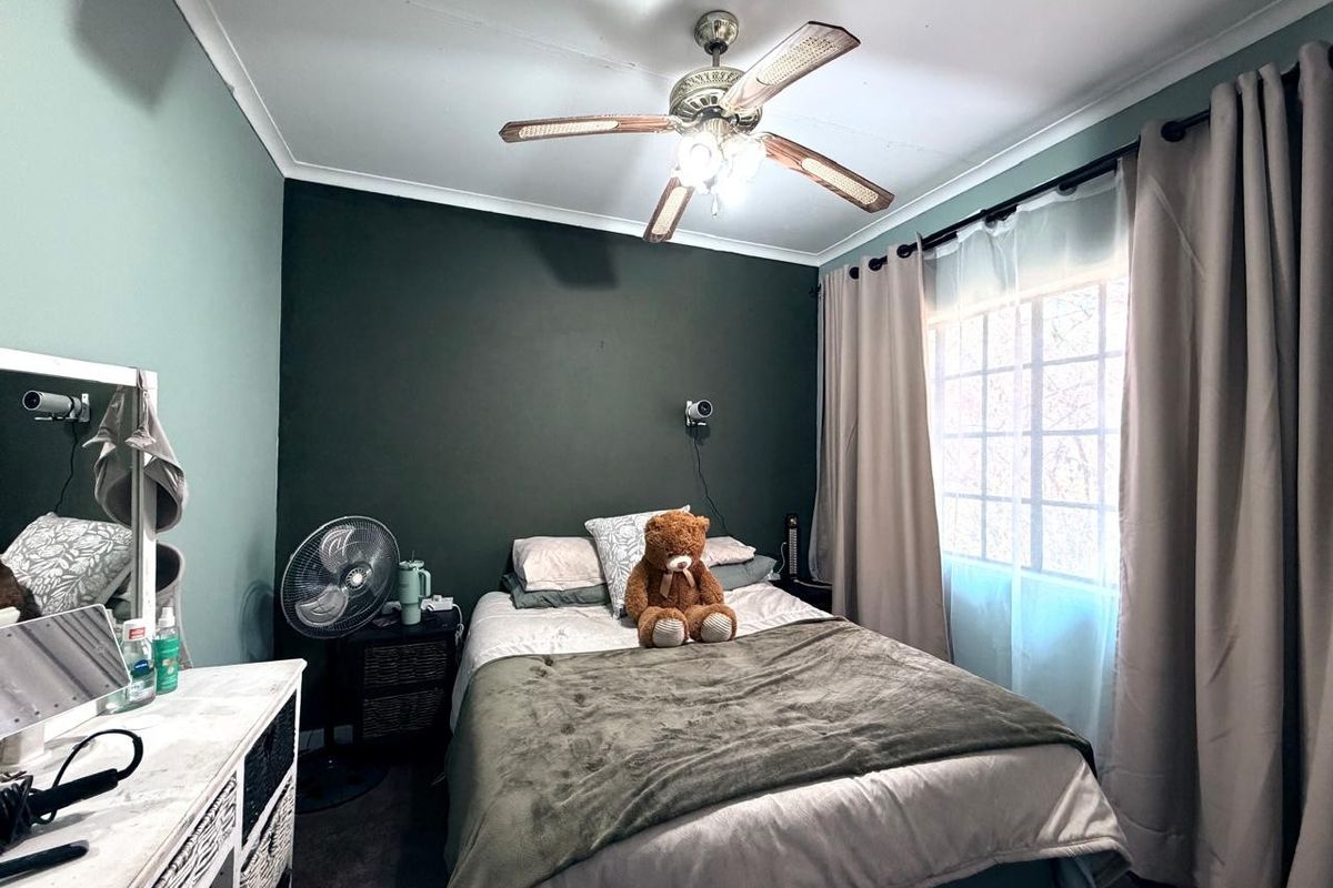 A cozy bedroom featuring a ceiling fan, dark accent wall, and window with curtains, providing a comfortable and functional sleeping space.