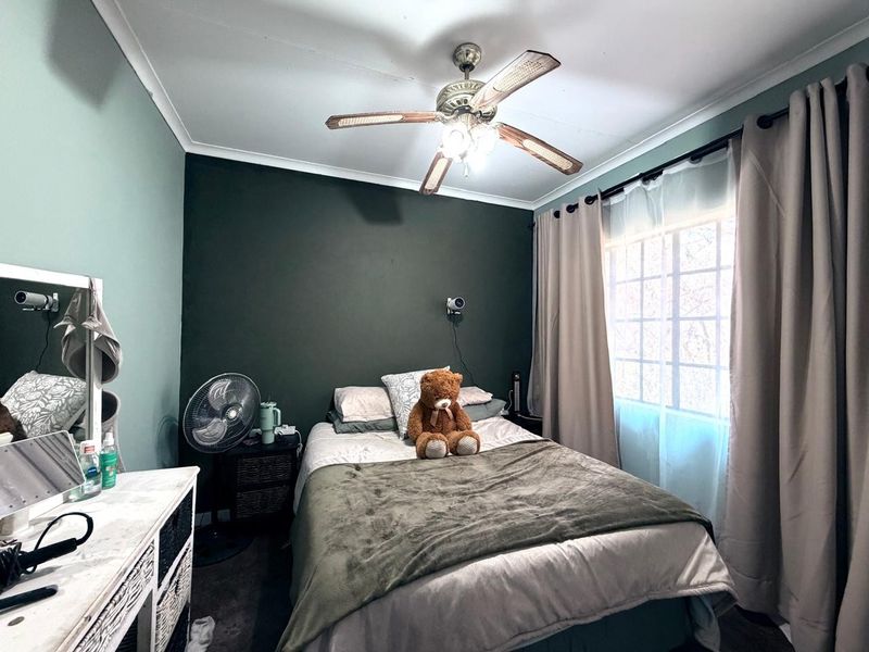 A cozy bedroom featuring a ceiling fan, dark accent wall, and window with curtains, providing a comfortable and functional sleeping space.