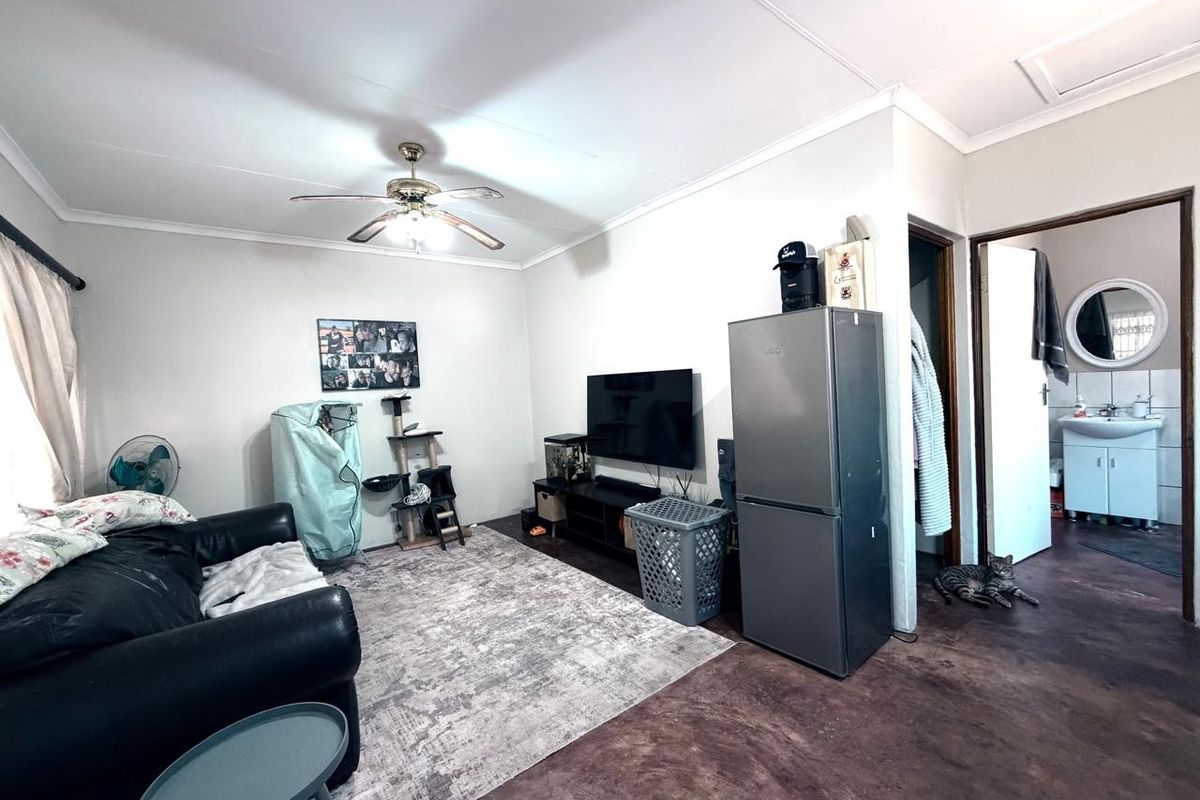 A functional living room area featuring a ceiling fan, coved cornicing, and direct access to an adjacent bathroom.