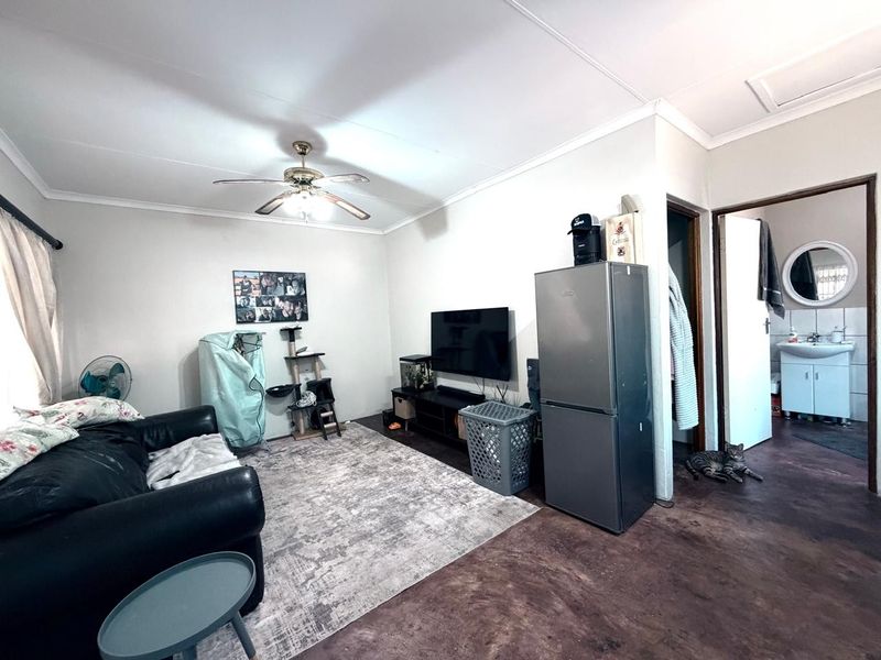 A functional living room area featuring a ceiling fan, coved cornicing, and direct access to an adjacent bathroom.