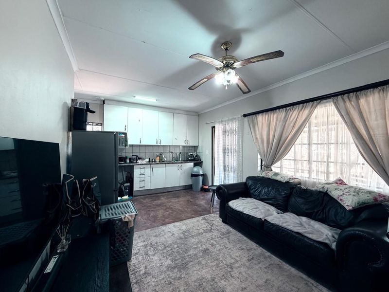 Open-plan living area featuring a compact kitchen with built-in cabinetry and a ceiling fan, seamlessly connected to the lounge space.