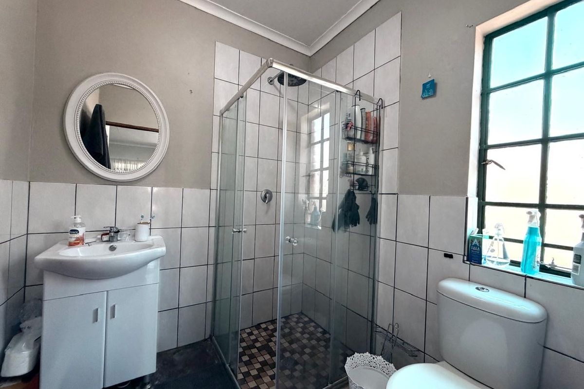 A functional bathroom featuring a glass shower enclosure, vanity basin, and toilet with tiled wall finishes and a steel frame window.