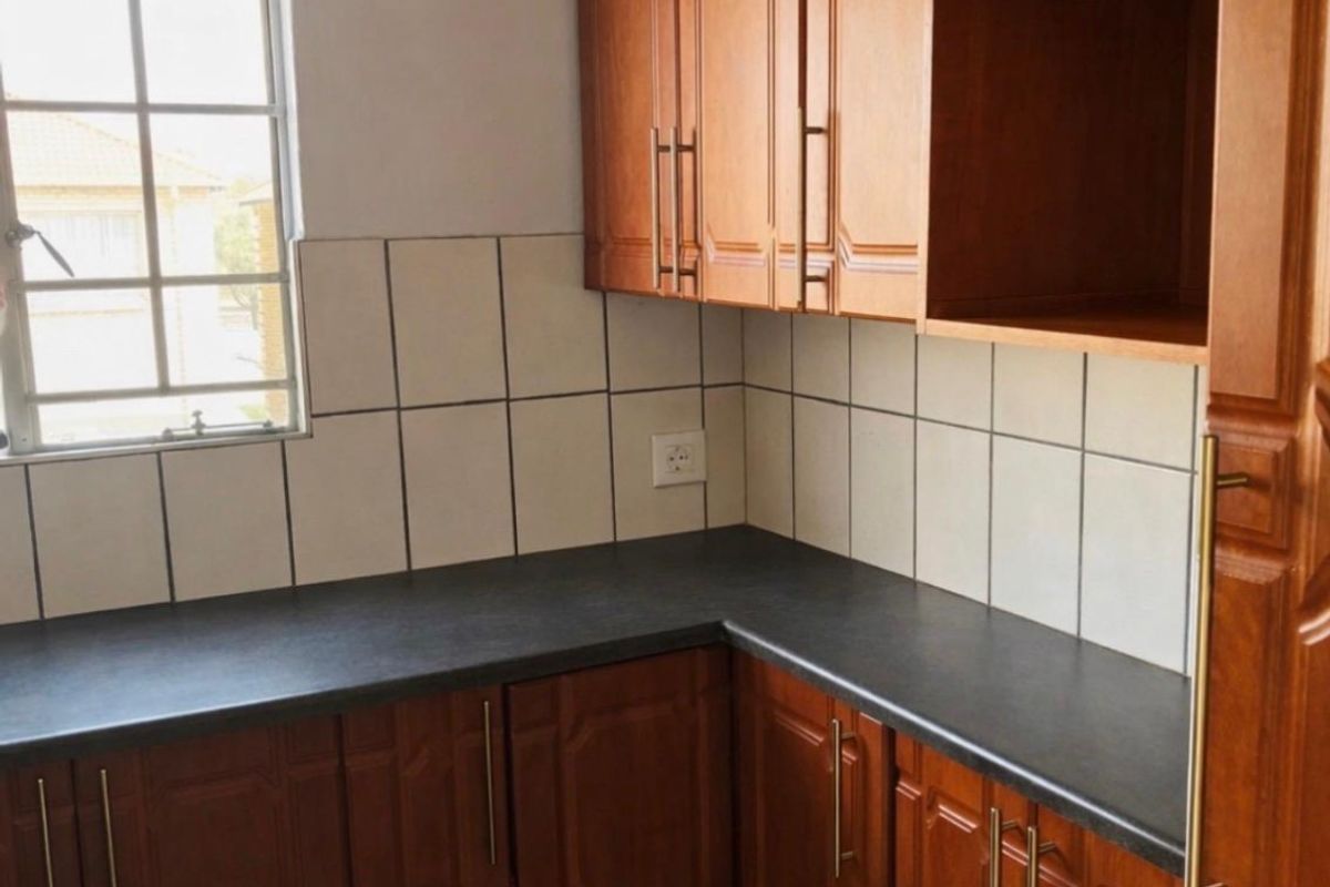 A functional kitchen area featuring wood-finish cabinetry, dark laminate countertops, and a tiled backsplash with a window for natural light.