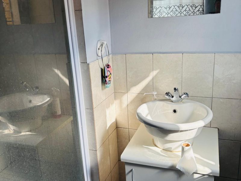 A functional bathroom featuring a vessel sink vanity, chrome mixer tap, and a glass-enclosed shower with tiled walls.